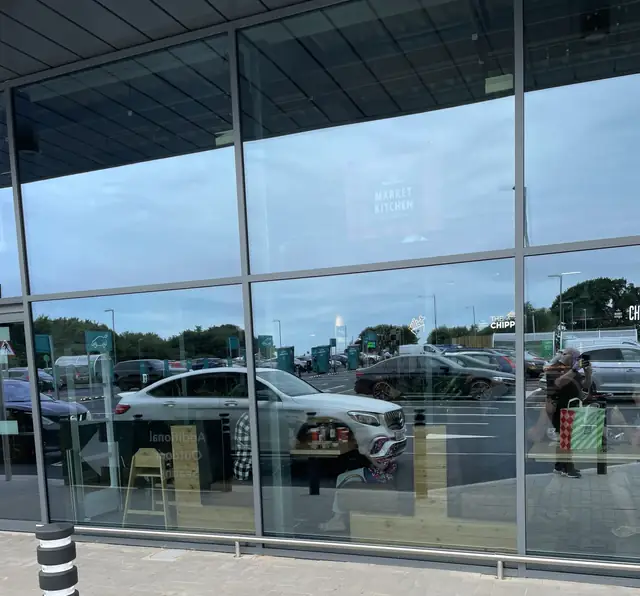 Supermarket glazed frontage reflecting the car park and the sky