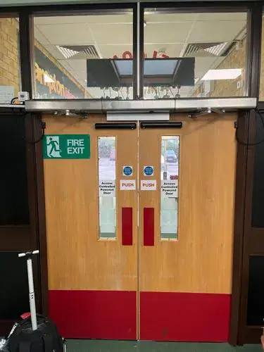 Timber faced fire exit double doors with push bars and a red kick plate