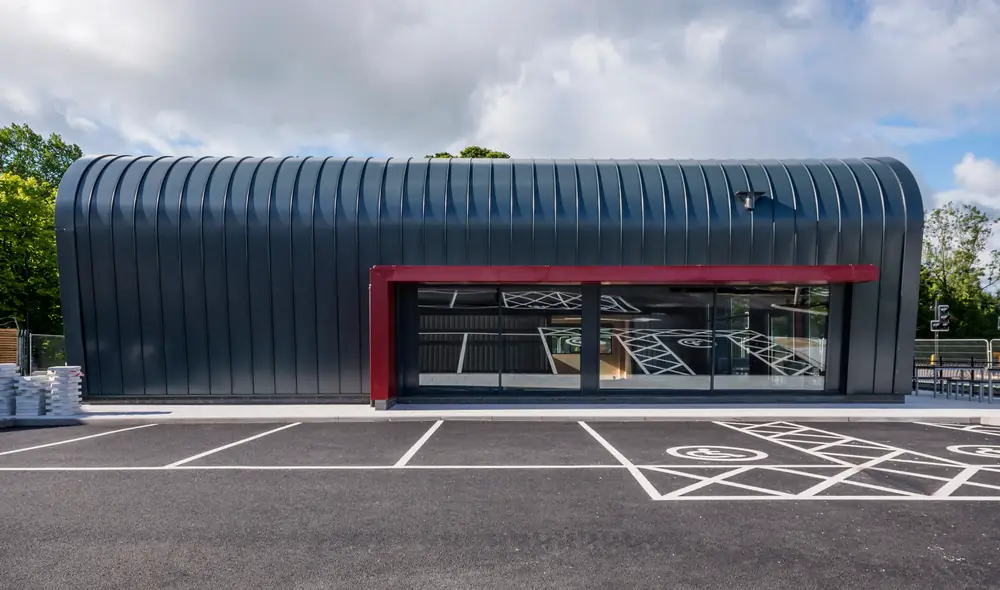 Finished Costa drive through unit with a curved dark standing seam roof and a crimson framed glazed frontage